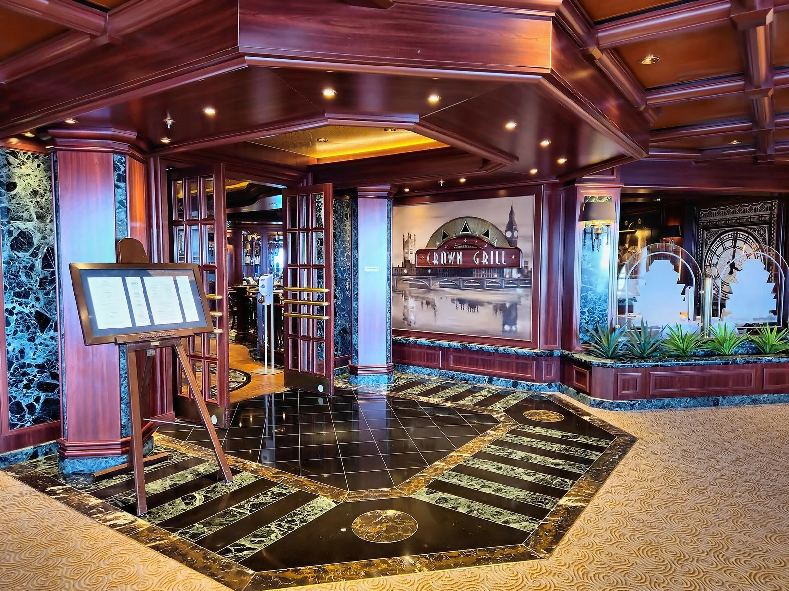 木の柱と大理石の床の入口に、CROWN GRILLの看板と献立の掲示が立つ。奥に店の席が見える。