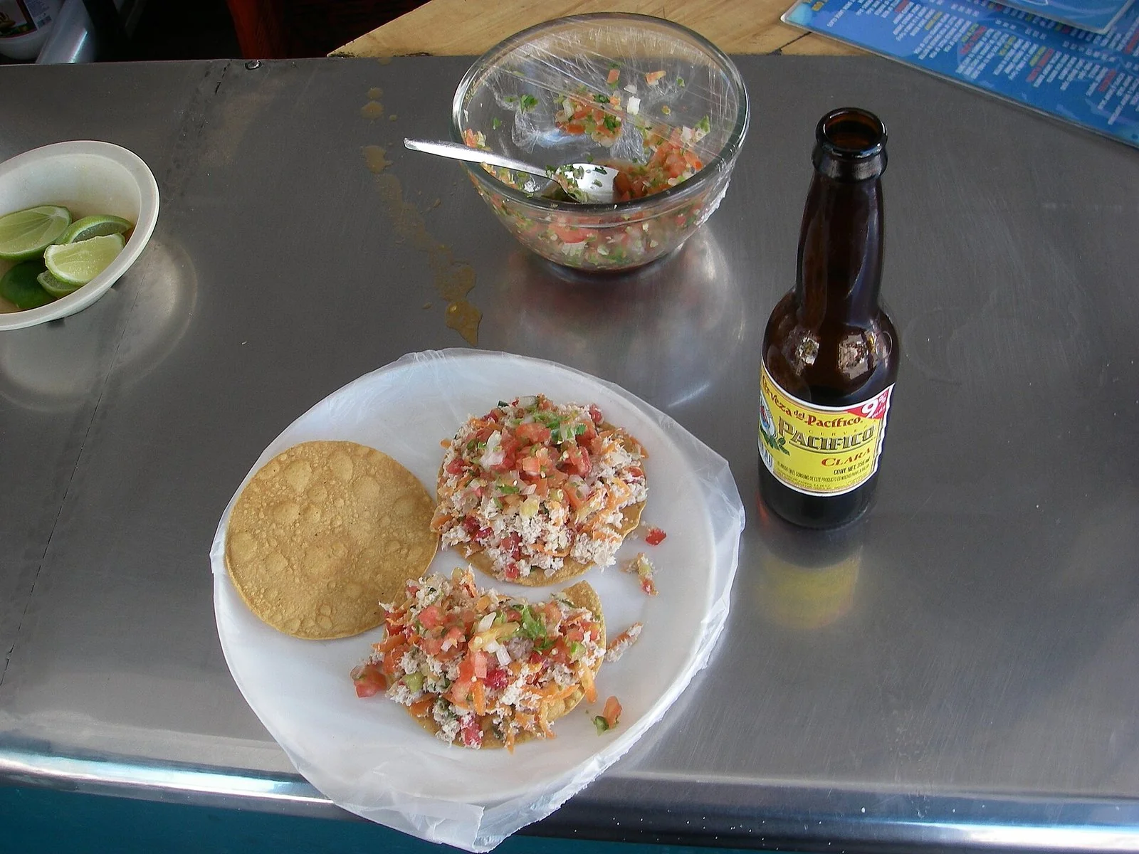 銀色のカウンターに、魚のセビーチェをのせたトスターダの皿とライム、サルサの器、ビールの瓶。