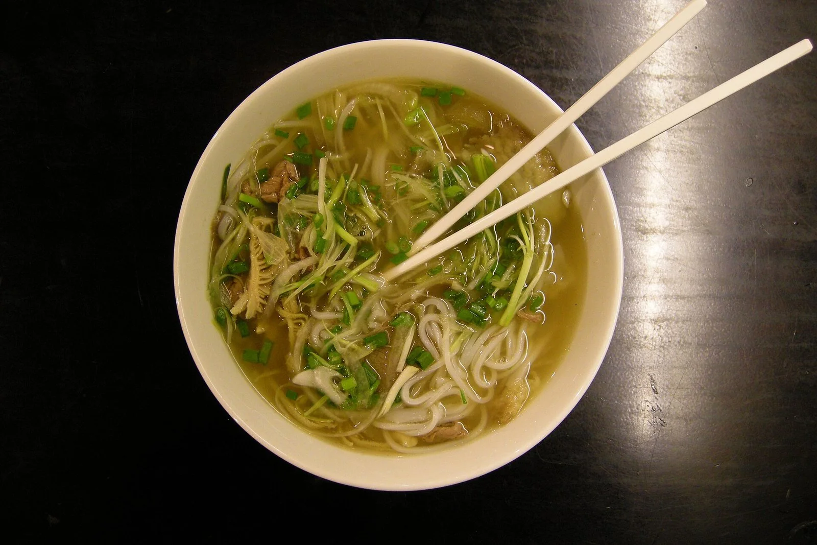 白い器に入ったフォー。米の麺と牛肉に、刻んだ青ねぎと香草がのる。