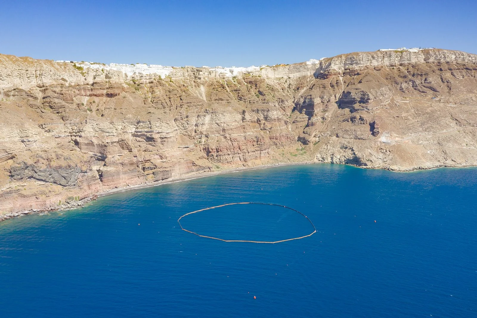 サントリーニ島の切り立った崖と青い海を上から見た眺め。崖の上に白い町。