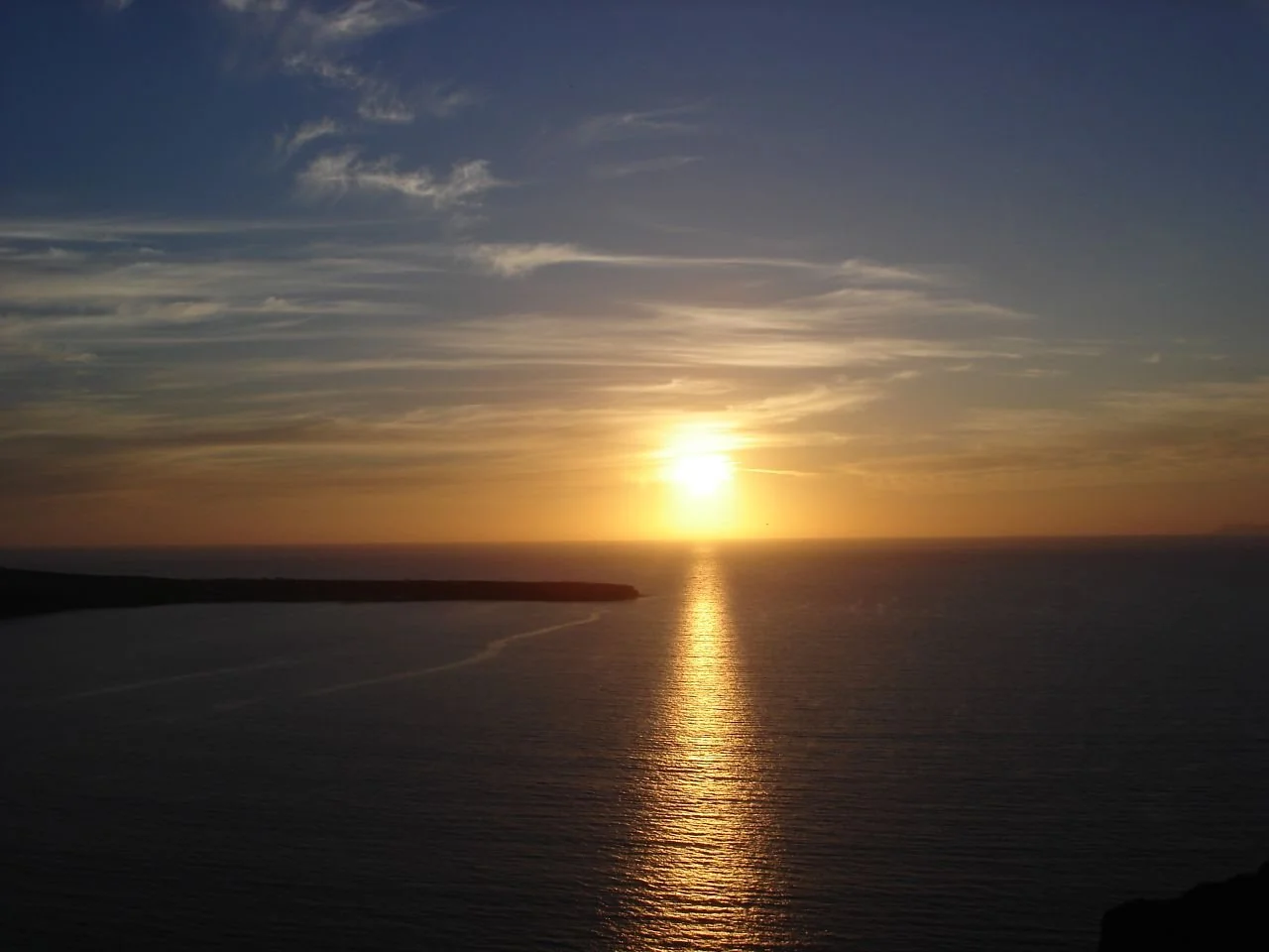 サントリーニ島オイアの岬の向こうに沈む夕日と、光る海。