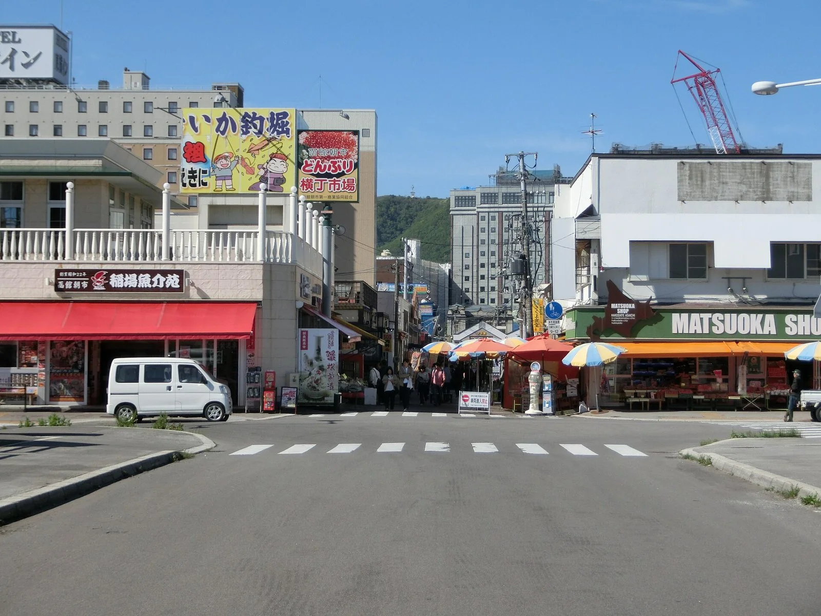 晴れた日の市場の通り。店の大きな看板と、道沿いに並ぶパラソルが見える。