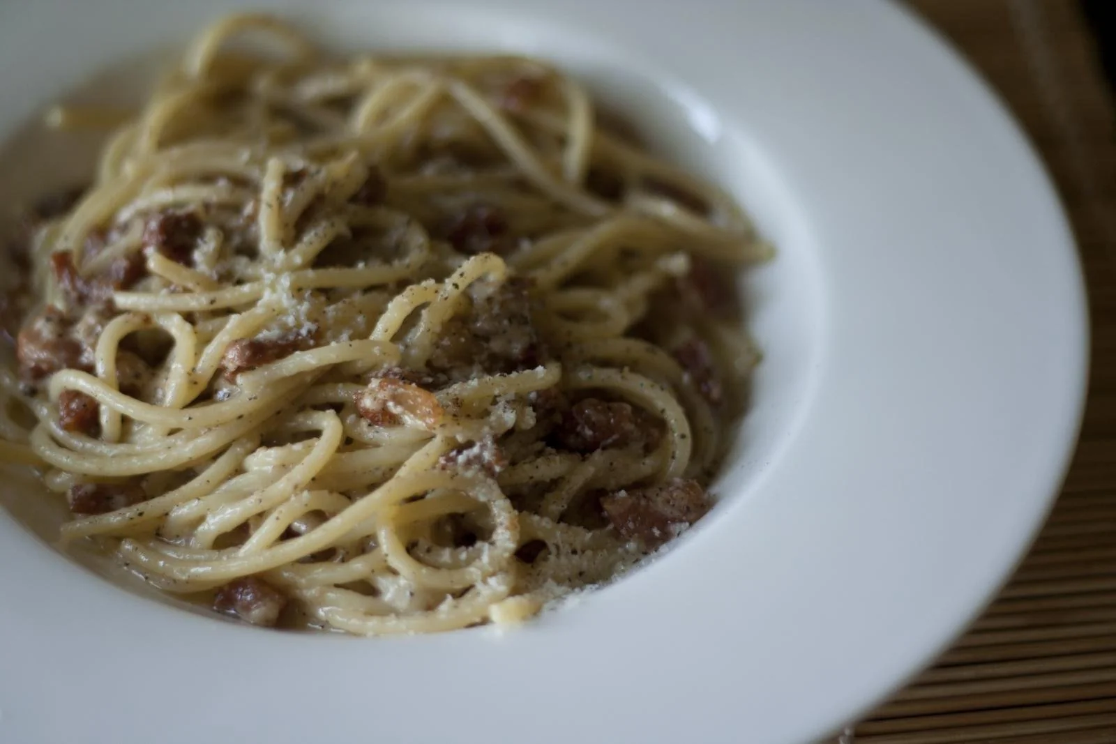白い深皿に盛ったスパゲッティ。角切りの豚のほほ肉とすりおろしたチーズ、黒こしょう。