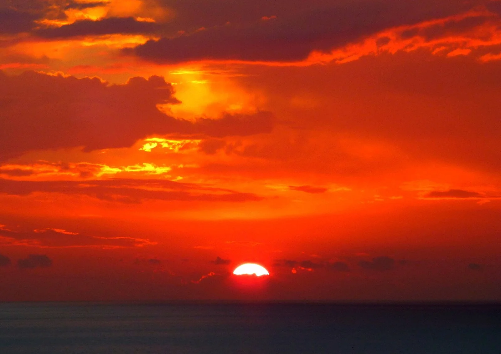 赤く染まった雲の下、水平線に半分沈んだ太陽と暗い海。